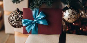 ajándékutalvány bordó borítékban kék masnival a karácsonyfa alatt karácsonyi ajándék